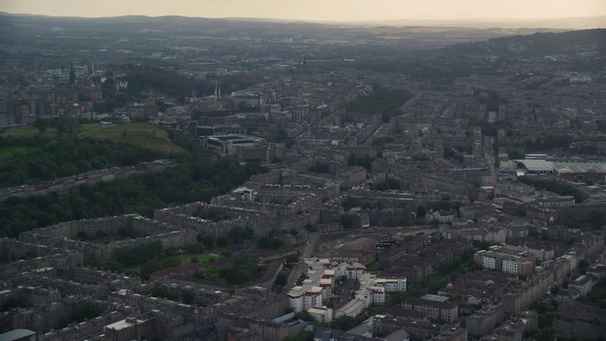 An aerial view of a metropolitan city with several buildings and a small hill with trees