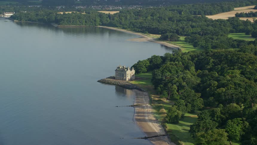 A secluded mansion near a huge lake is surrounded by big treesand vast field