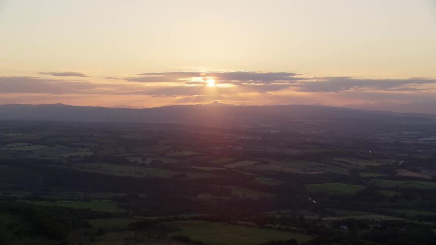 Aerial of the sun behind clouds above the horizon casting rays over a grass land