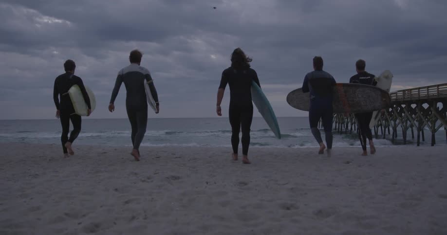 A group of people walk on the beach towards the water holding surfboards
