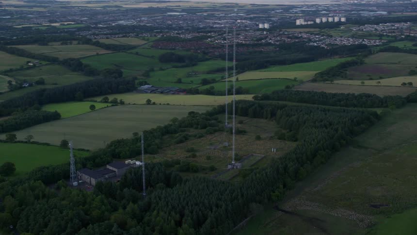 Some power towers in an empty field with grass and in the background a city
