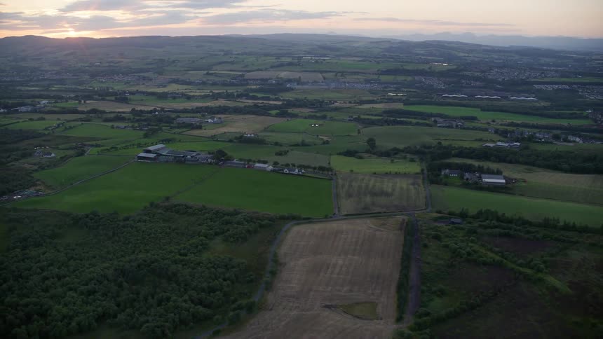 Several fields of grass in a field with a few small houses