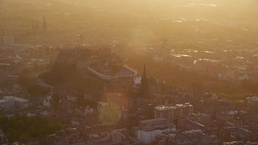 Aerial of city buildings as the sun rises on the horizon casting rays across the cityscape