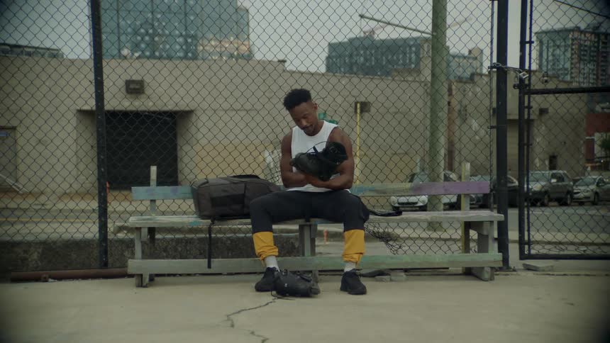 A man sitting on a wooden bench pulls out a pair of skates from his bag