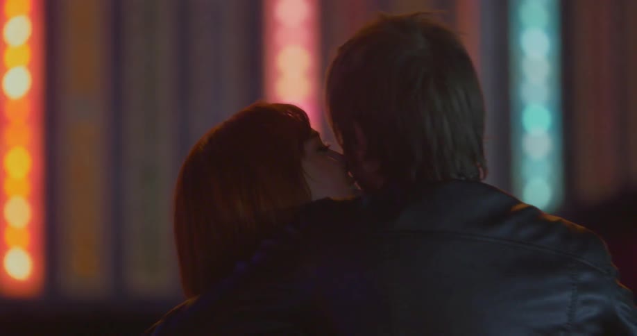 Man and woman embrace in front of blinking colored lights