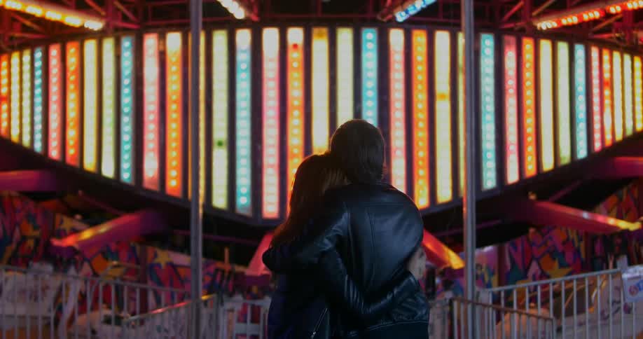 A man and woman embrace in front of many different colored lights