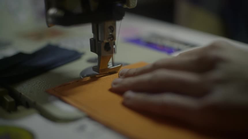 A person slowly moves a piece of fabric underneath the needle of a sewing machine