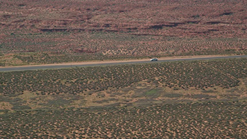 Aerial view of white car driving on highway in the desert