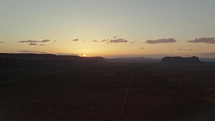 A desert region with mountains in the background and the sun rising in the sky