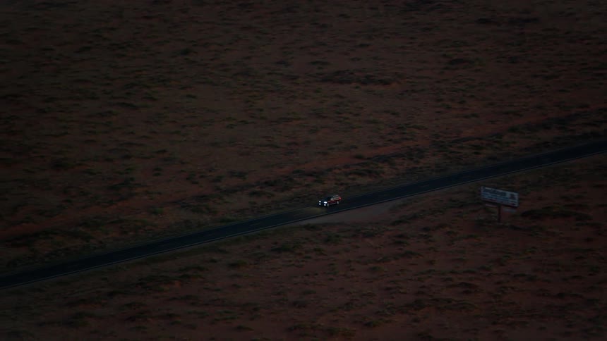 A car drives along a remote road that is lined with large fields