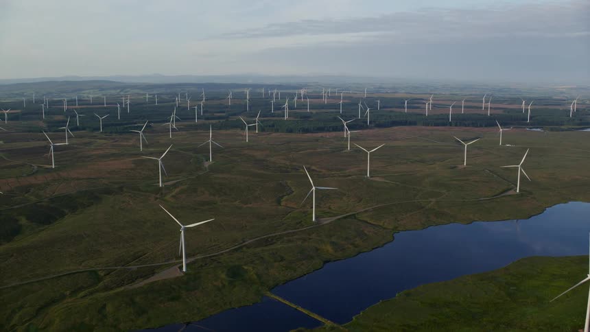A road runs through a wind farm near a small lake as wind turbines stand tall across the landscape