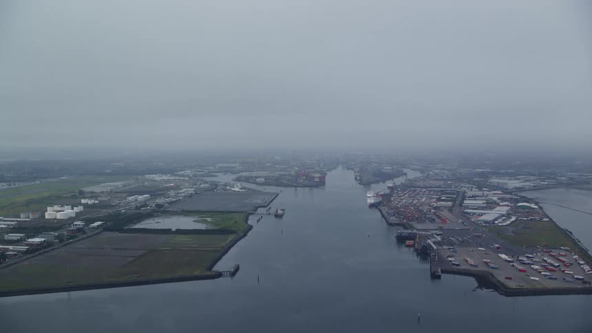 Aerial view of a sea and waterway with vehicles parked around on a cloudy day