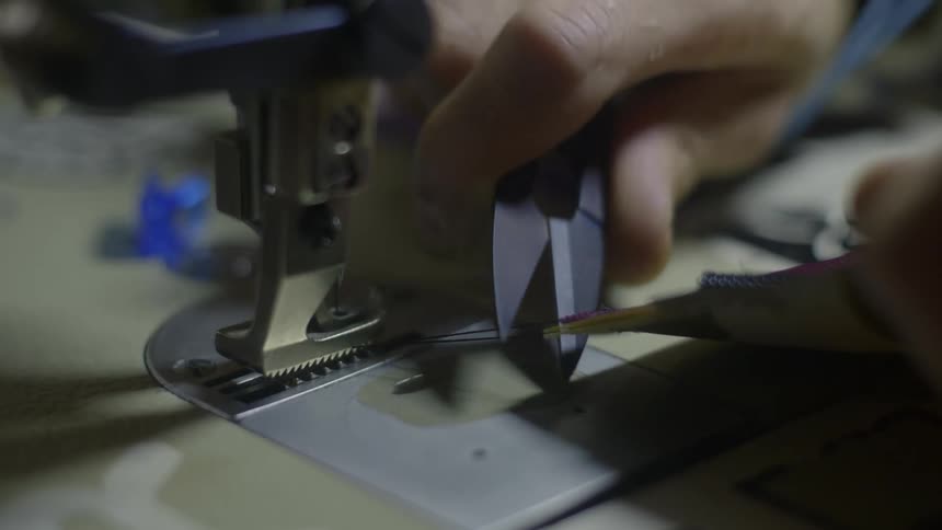 Hand holding scissors snips thread near sewing machine