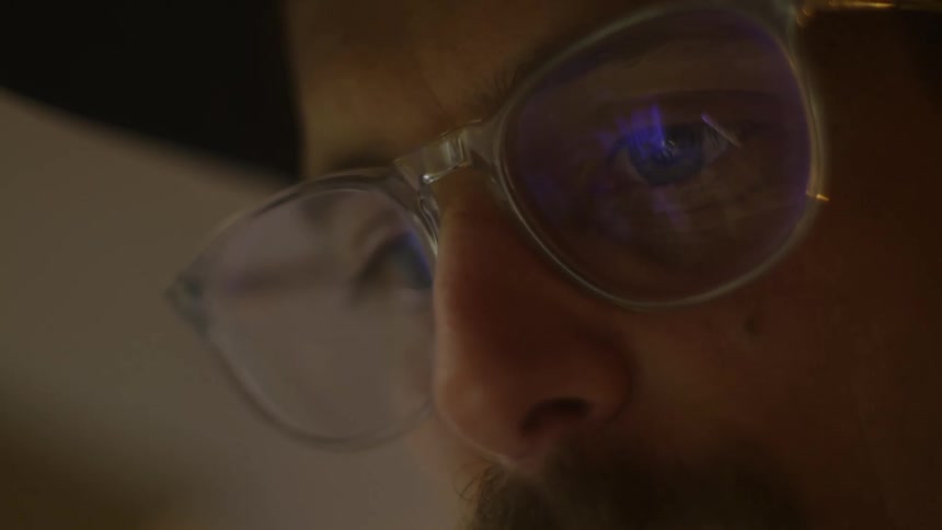 Close up of the face of a man wearing glasses looking at a screen