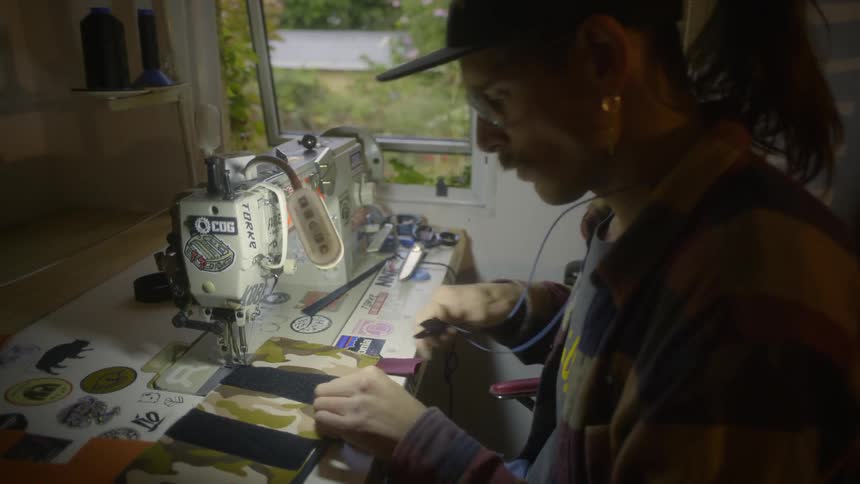 Tailor with cap ponytail mustache and plaid shirt uses sewing machine