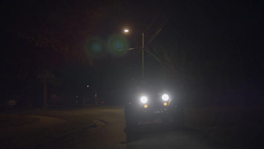 A jeep drives down the street at night