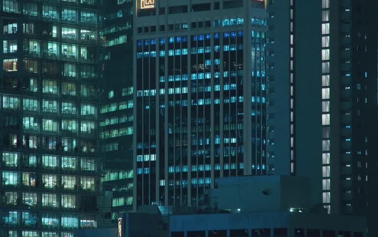 Lights turning on in the windows of city buildings