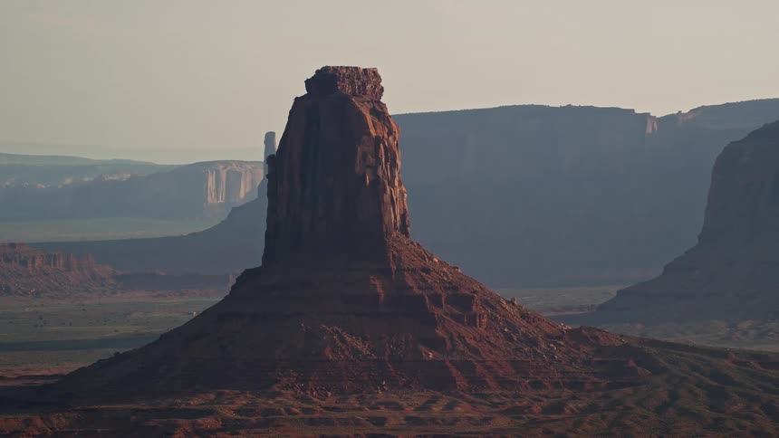 Aerial of a butte formation in the desert as the sun shines on it casting shadows behind