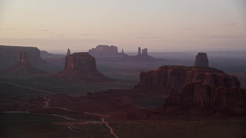 A desert region with canyons and rocky mountains and a sand road crossing the terrain