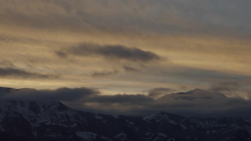 Lowhanging clouds above a snowy mountain range at sunrise