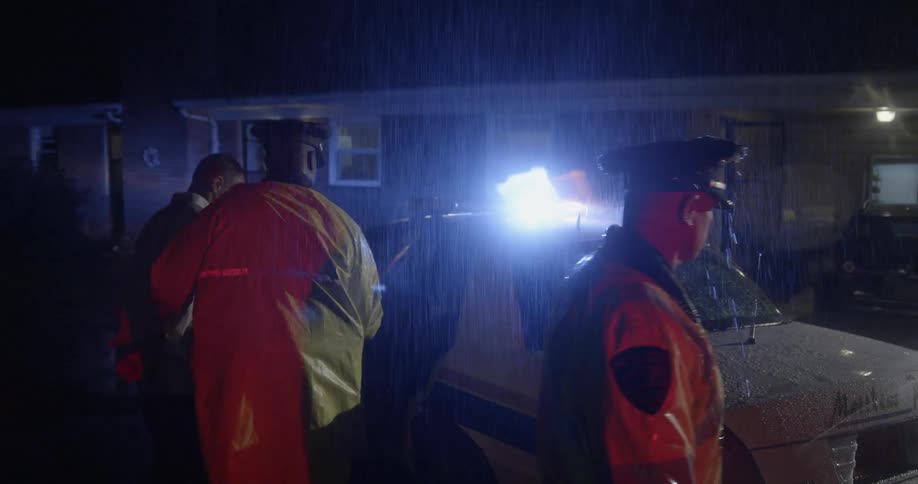 Officers walk outside in the rain at night