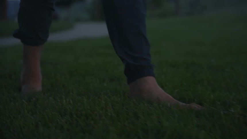 Man walks away from sidewalk through grass barefoot