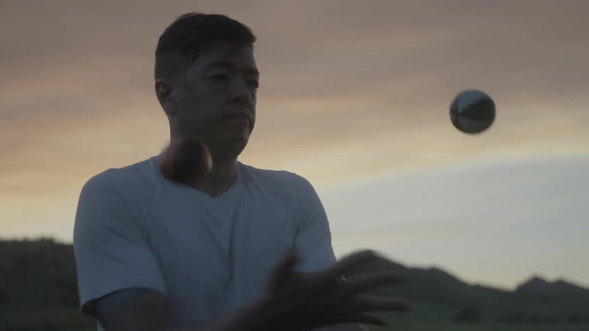 Man juggles balls while standing outdoors near hills at sunset