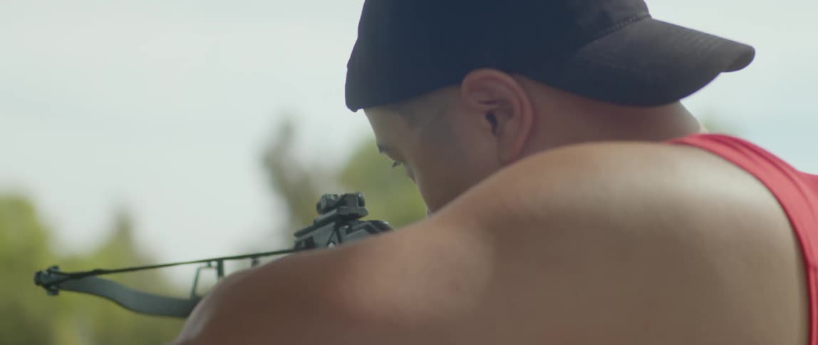 A man slowly draws a crossbow as he raises it to aim at a target