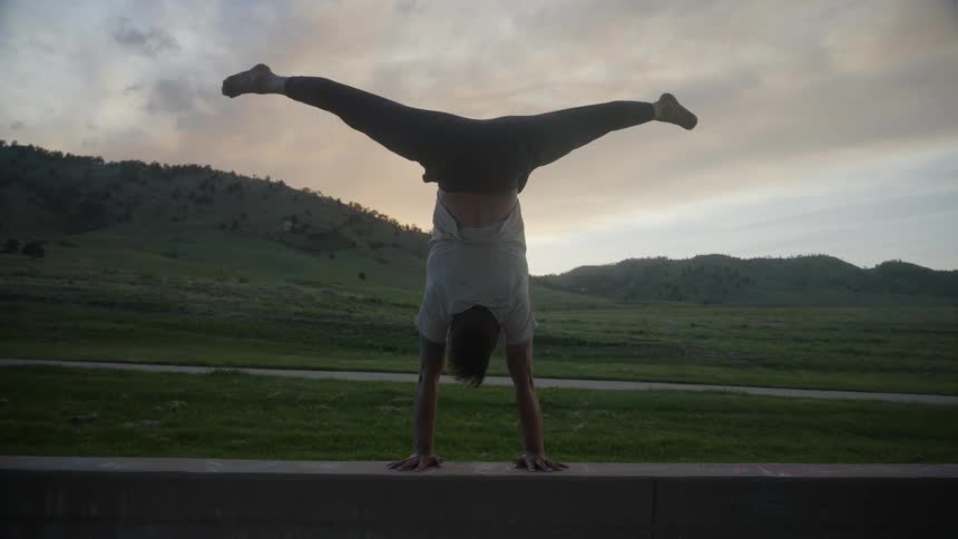 A man exercising alone outside in a keg stand position at sunset