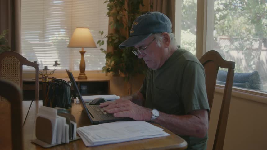 An elderly person in their office typing on their laptop
