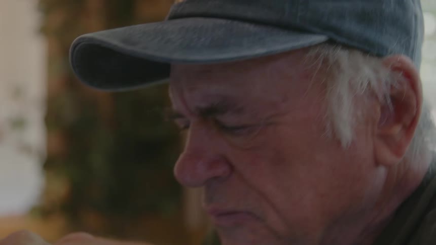 An elderly man takes off his glasses and types on a laptop computer