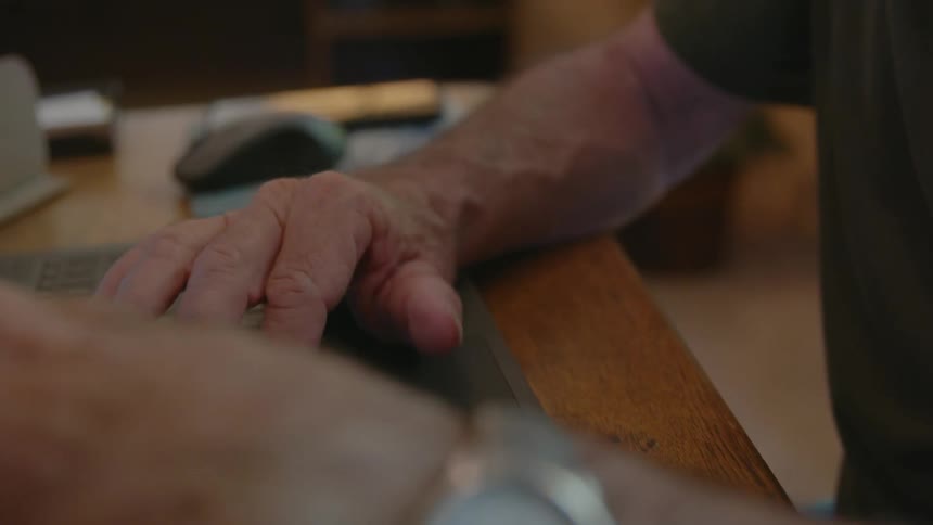 An elderly man typing on a laptop