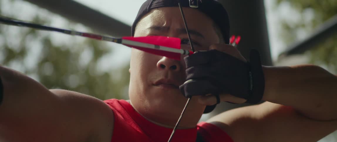 A man pulls back his bow looking ahead as he releases the arrow