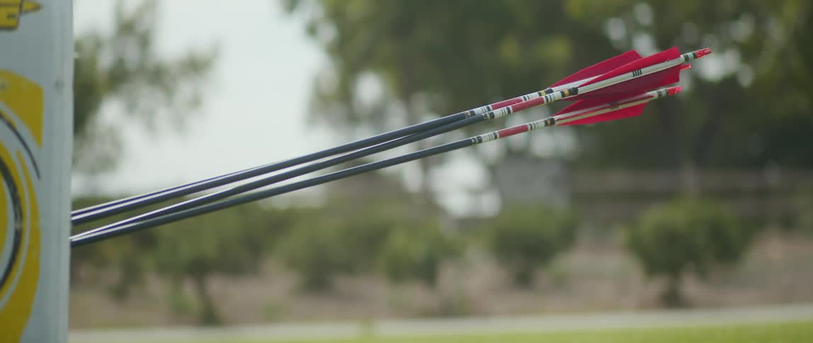 An arrow strikes an archery target that is located outdoors
