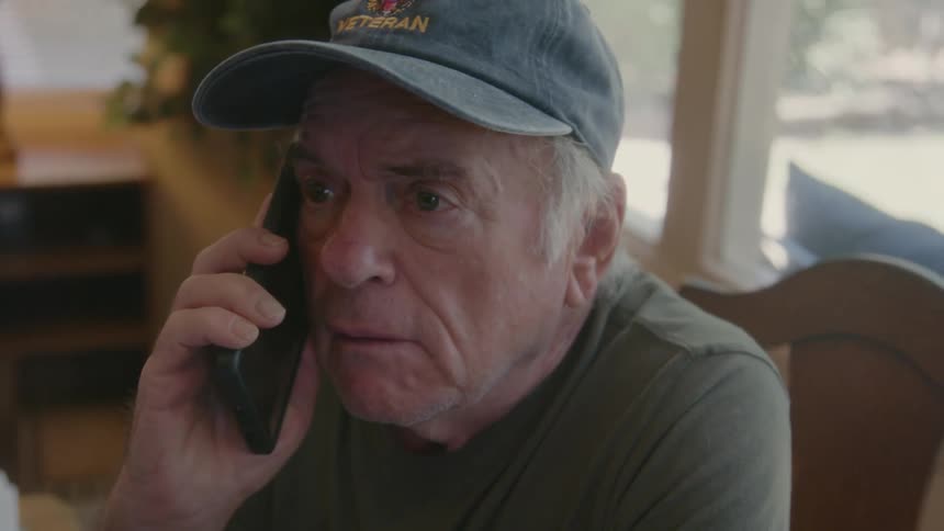 Elderly person sitting talking on the phone with a facial expression of irritation