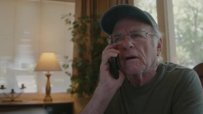 An elderly person sitting and talking on the phone with a facial expression of indignation