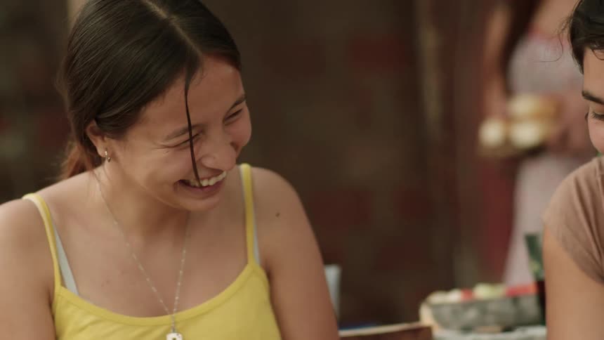 One woman shows the other something on her cell phone and they both laugh as they sit down