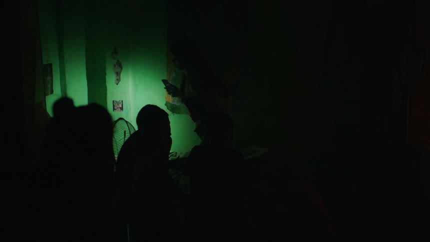 A dark room with a lit candle and a person illuminating the path they are walking with a cell phone flashlight