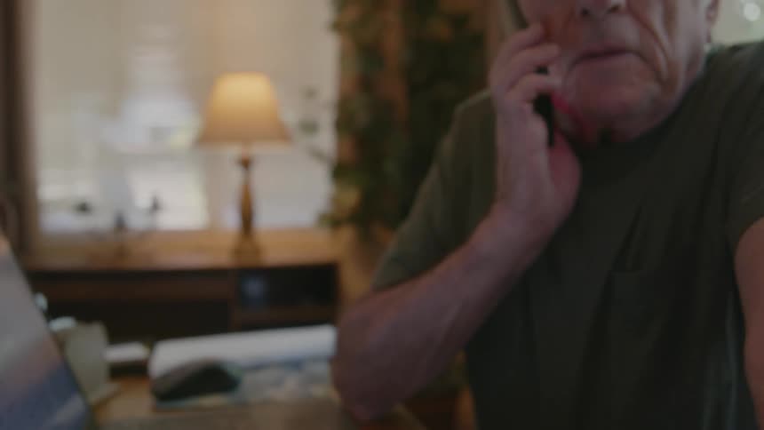 An elderly man types on a cell phone and brings it to his ear