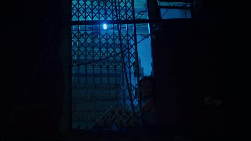 A person sits on the ground next to a railing and under a blue light