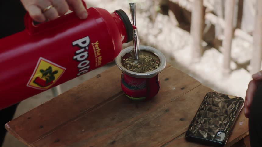 Closeup of a persons hands preparing mate tea and handing it to another person