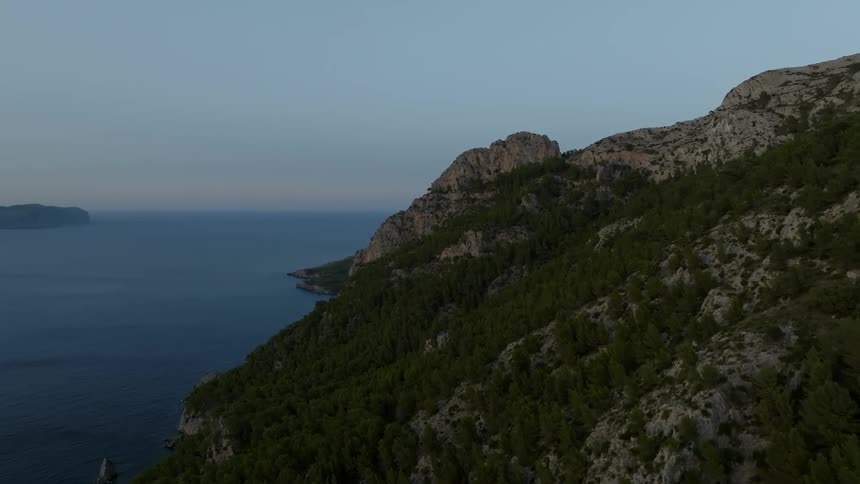 A mountain with rocks and vegetation and in the background there is a horizon of a huge ocean