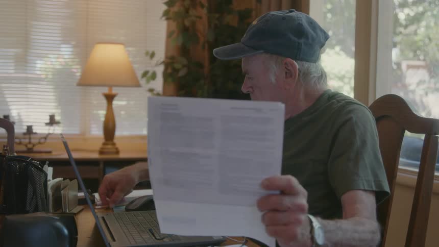 Elderly man sits at table making notes after reading document