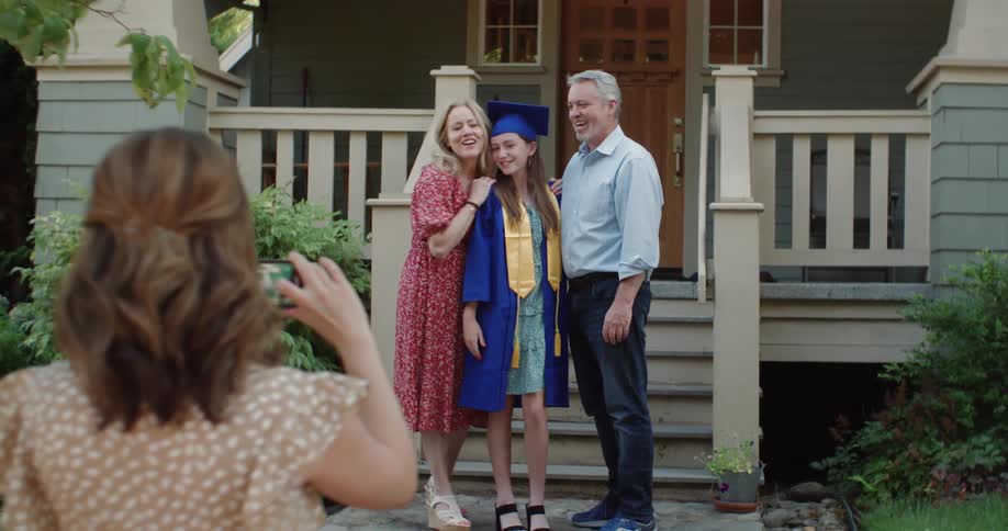 A teenage girl dressed in graduation gown posing for a photo with her parents for high school graduation
