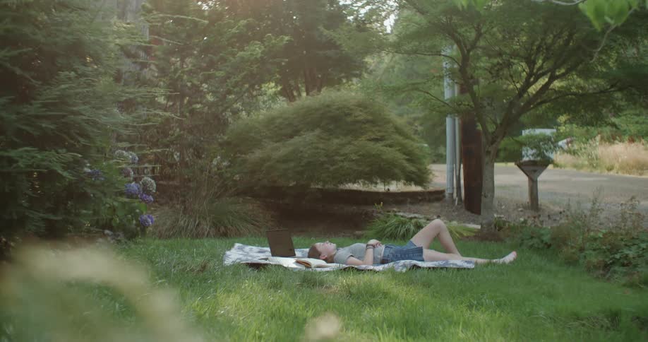 A teenage girl lies on a blanket in the yard on a summer day