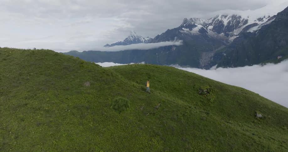 Aerial of hiker with yellow coat and black backpack walks down mountain slope
