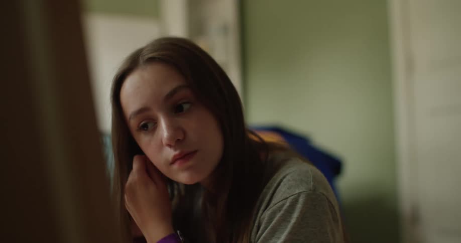 A teenage girl is putting on earrings while sitting in front of the mirror