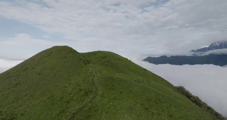 A hiker ascends a mountain peak covered in low vegetation during the day