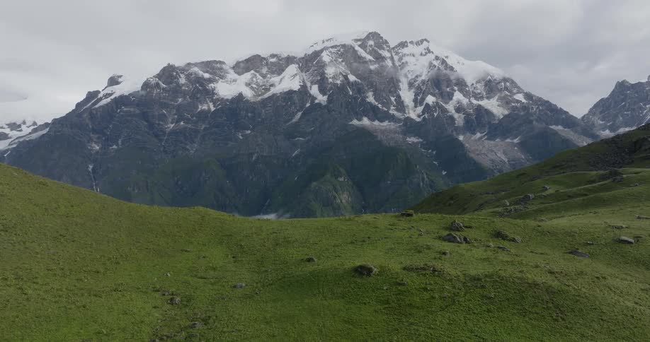 Aerial view of hiker walking down green mountain with snowy mountain range in the background