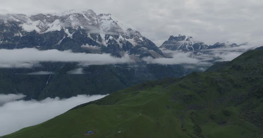A grassy hill surrounded by snowcapped mountains